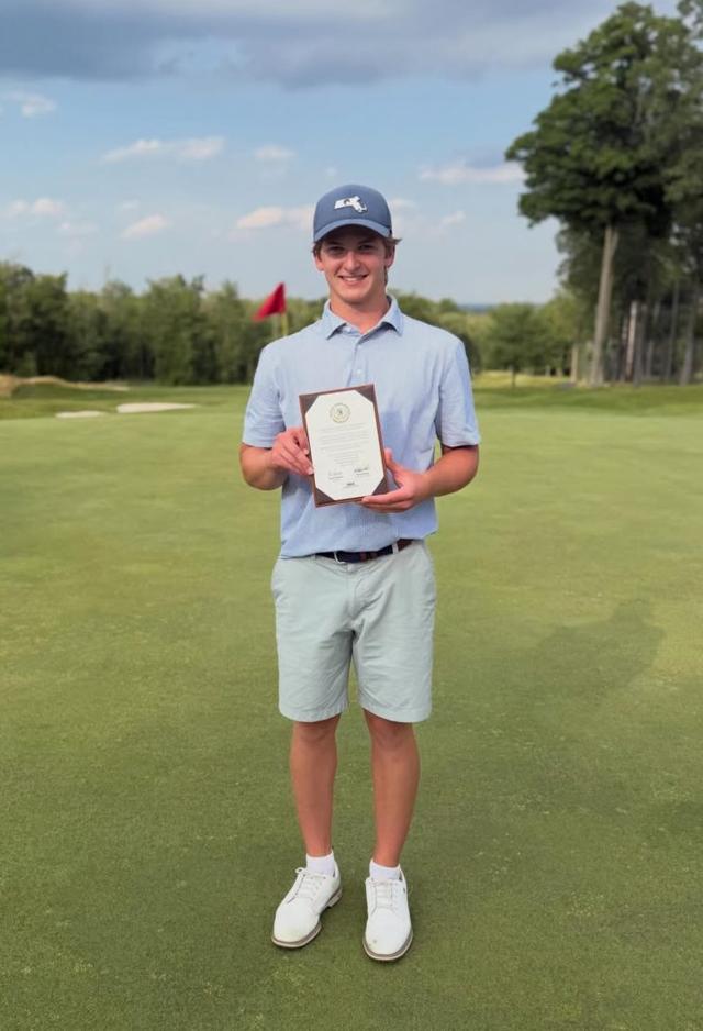 Student Maxx Zides standing on a putting green holding his framed U.S. Junior Amateur qualifying certificate