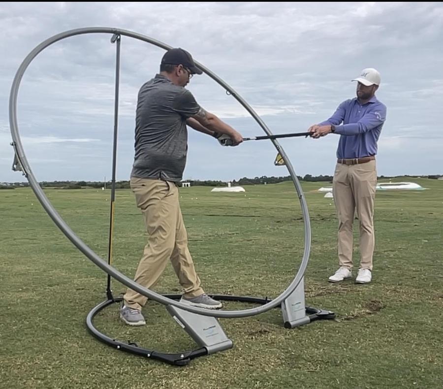 Instructor guiding a student's club through a swing plane training aid on the range